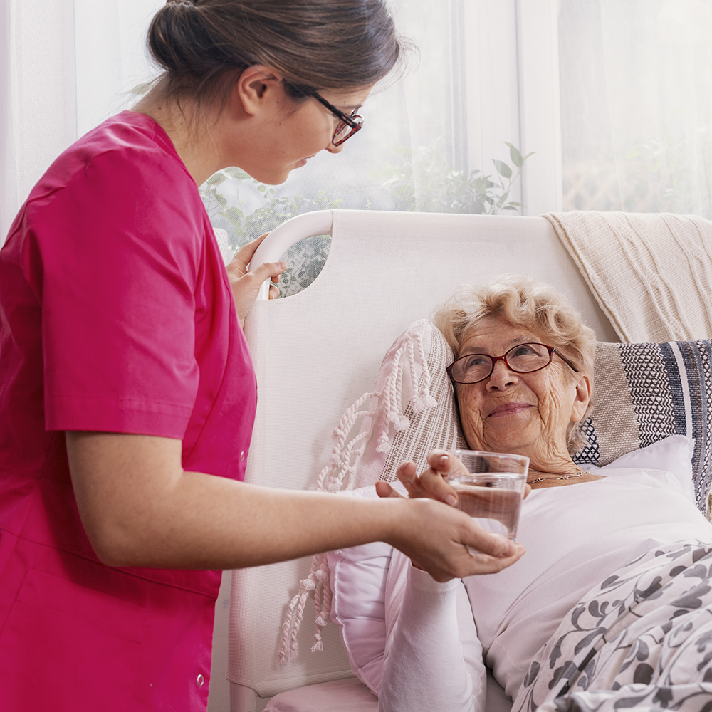 Beautiful young nurse serves tea to an elderly lady in a private