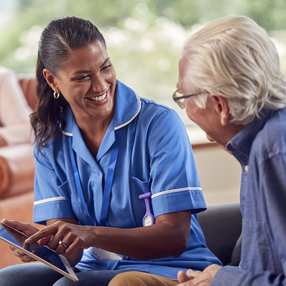 Senior Couple At Home With Man Talking To Female Nurse Or Care W
