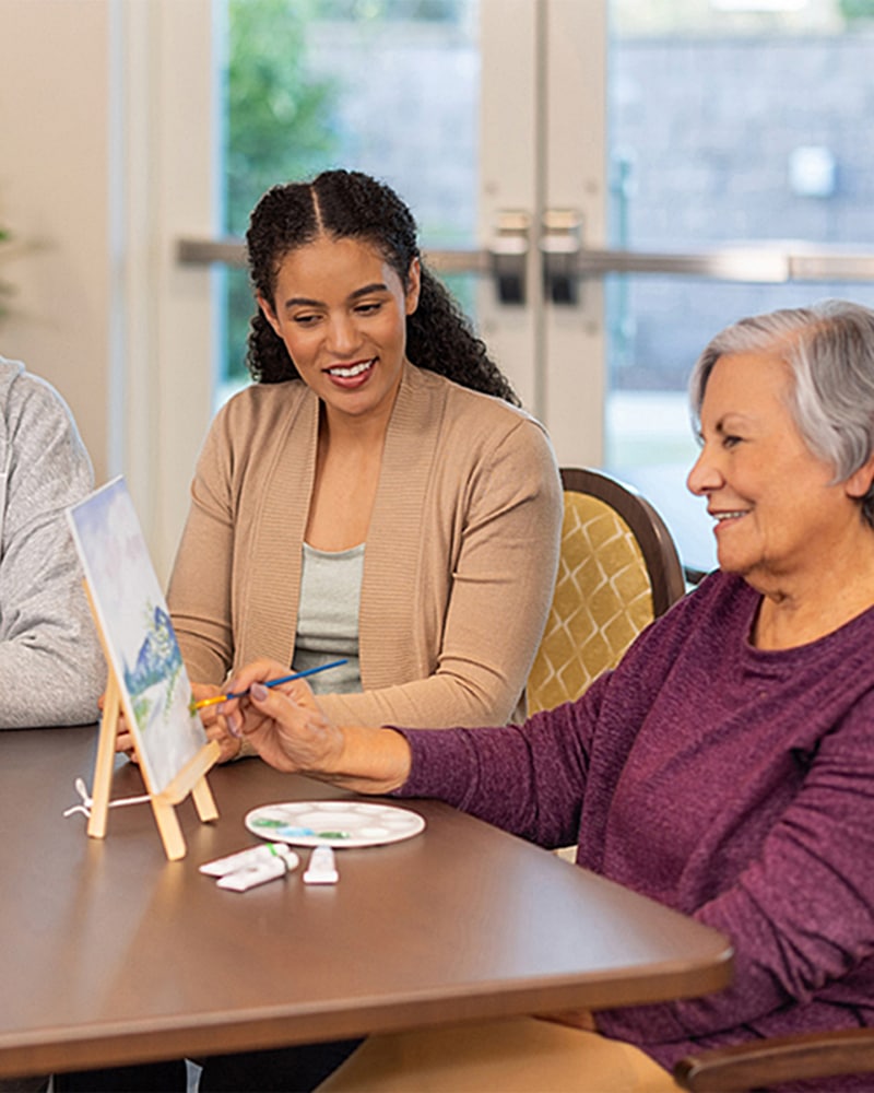 a woman helps an elderly woman work on a painting