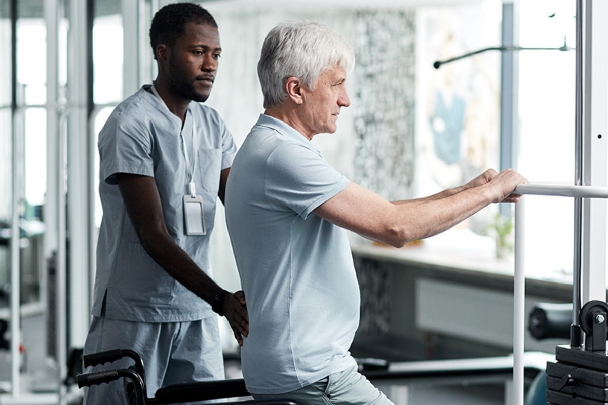 Care professional assisting an older man with mobility exercises
