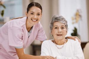 Caregiver in pink scrubs smiling with an older woman seated in a wheelchair